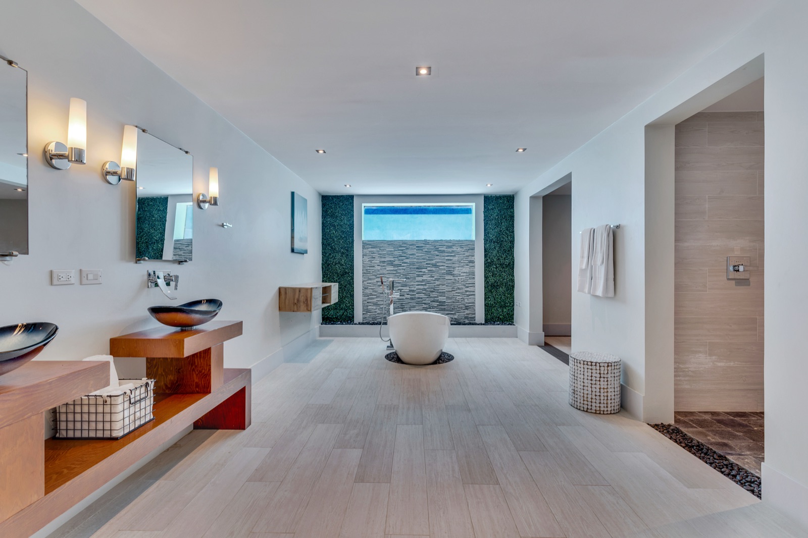 Luxury Bonaire villa spa bathroom featuring a freestanding soaking tub with an underwater pool window view, custom wood double vanities, and a walk-in shower.